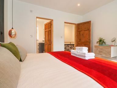 A bedroom with a bed red and orange blanket open wooden doors and a wooden dresser with plants at Yamthwaite in Grizedale near Hawkshead