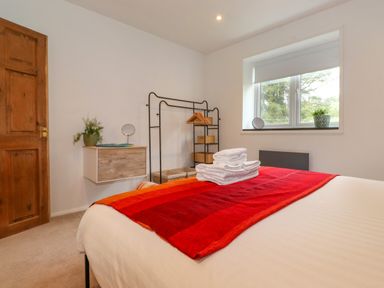 A bedroom with a bed with folded towels on a red blanket a wooden door a wall-mounted cabinet a clothing rack and a window with plants at Yamthwaite in Grizedale near Hawkshead