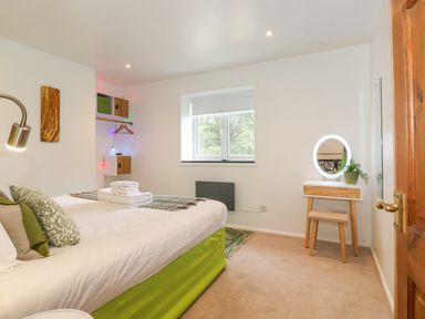 A bedroom with a bed green bedding a vanity table with mirror and stool and a window at Yamthwaite in Grizedale near Hawkshead