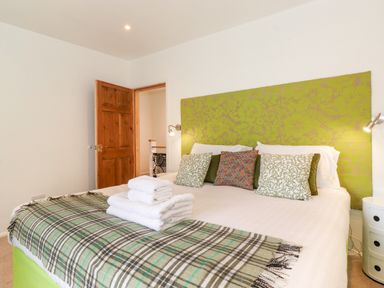 A bedroom with a bed with green patterned headboard and cushions with towels on the bed at Yamthwaite in Grizedale near Hawkshead