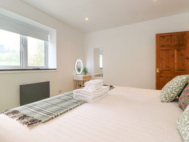 A bedroom with a bed folded towels a bedside table with a round mirror and plants and a wooden door at Yamthwaite in Grizedale near Hawkshead