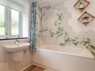 A bathroom with a bathtub shower combination a sink and hexagonal tiles with leaf patterns at Yamthwaite in Grizedale near Hawkshead