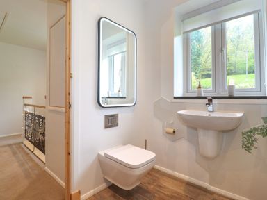 A bathroom with a wall-mounted toilet and sink under a window at Yamthwaite in Grizedale near Hawkshead