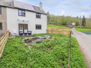 A backyard garden with a small pond and two chairs on a wooden deck at Yamthwaite in Grizedale near Hawkshead