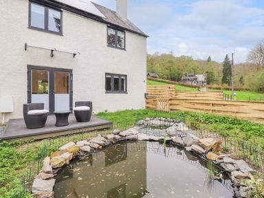 A garden with a pond and patio furniture outside a house at Yamthwaite in Grizedale near Hawkshead