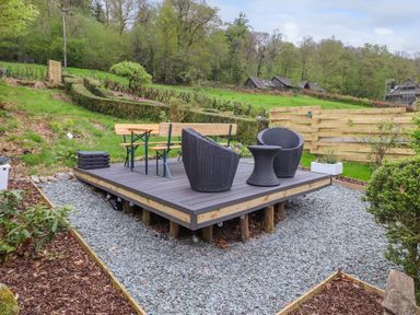 A raised wooden deck with chairs and a table in a garden with gravel and hedges at Yamthwaite in Grizedale near Hawkshead