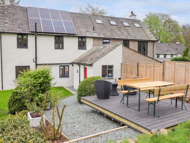 An outdoor patio area with wooden table and benches on a raised platform in the garden of a house with solar panels on the roof at Yamthwaite in Grizedale near Hawkshead