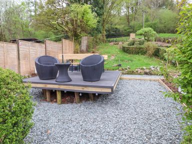 A garden area with wicker chairs and a table on a raised wooden platform surrounded by gravel at Yamthwaite in Grizedale near Hawkshead