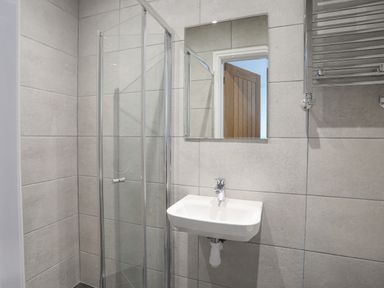 A bathroom with a glass shower enclosure a wall-mounted sink a mirror and a towel radiator at The Hawthorns in Llanfechell