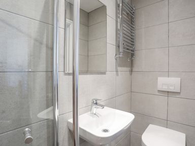 A bathroom with a white sink and faucet a glass shower enclosure a wall-mounted mirror a chrome towel radiator and a toilet at The Hawthorns in Llanfechell