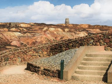 A stone wall and steps in a rocky desert landscape with a tower on a hill in the background at The Hawthorns in Llanfechell