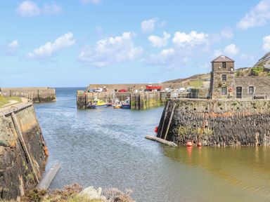 A harbor with fishing boats and a stone building near the water at The Hawthorns in Llanfechell
