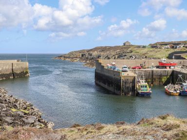 A small harbor with boats docked near a concrete pier and rocky coastline at The Hawthorns in Llanfechell