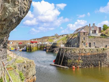 A small harbor with boats docked near stone buildings and a rocky shoreline at The Hawthorns in Llanfechell