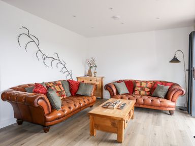 A living room with two brown leather sofas red and gray cushions wooden coffee table and cabinet with flower vase at The Hawthorns in Llanfechell