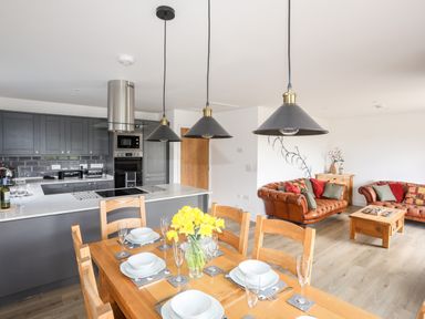 A kitchen with grey cabinets and a wooden dining table set with white dishes and a vase of yellow flowers at The Hawthorns in Llanfechell