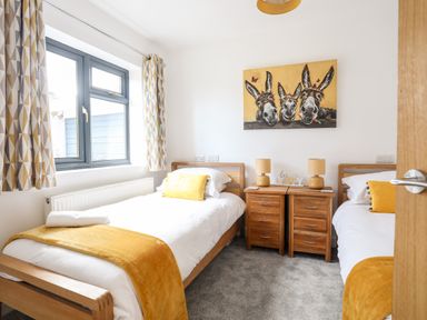 A bedroom with two single beds wooden bedside tables lamps and a painting of three donkeys at The Hawthorns in Llanfechell