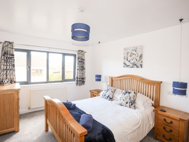 A bedroom with a wooden bed frame two bedside tables a dresser blue lampshades and patterned curtains at The Hawthorns in Llanfechell