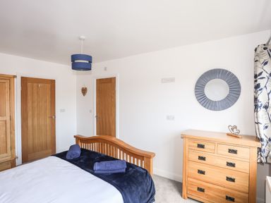 A bedroom with wooden bed frame and chest of drawers two doors and a circular wall mirror at The Hawthorns in Llanfechell