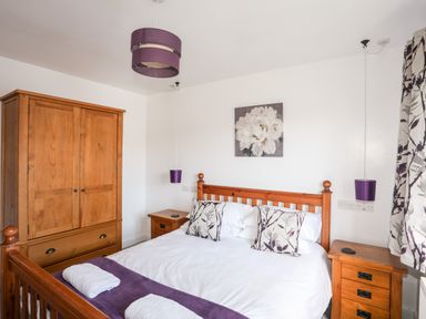 A bedroom with a wooden bed and wardrobe white bedding and purple accents at The Hawthorns in Llanfechell