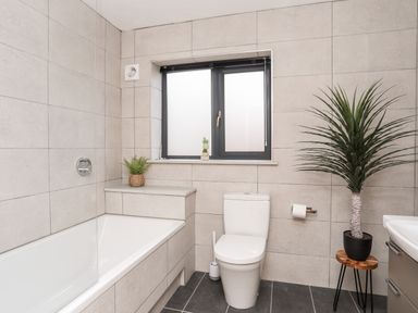 A bathroom with a bathtub toilet window and plants at The Hawthorns in Llanfechell