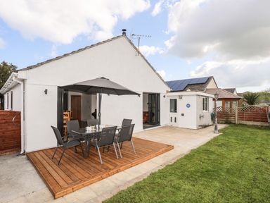 A patio area with outdoor dining furniture and an umbrella next to a white house with a garden at The Hawthorns in Llanfechell