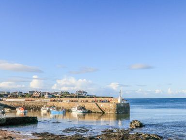 A small harbor with boats docked near a stone pier and houses in the background at The Hawthorns in Llanfechell