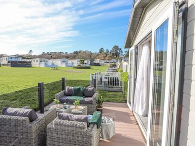 A patio with outdoor wicker furniture and cushions outside homes with green lawns at 97 Crugan in Llanbedrog