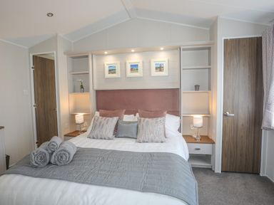 A bedroom with a double bed two lamps on side tables and three framed pictures above the headboard at 97 Crugan in Llanbedrog