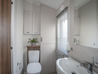 A bathroom with a toilet a sink cabinets a small plant and a window with blinds at 97 Crugan in Llanbedrog