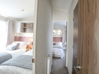 A hallway with a door on the right leading to a bedroom with two single beds and another bedroom visible at the end with a double bed at 97 Crugan in Llanbedrog