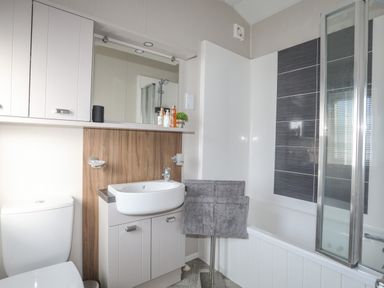 A bathroom with a toilet sink mirror towel and bathtub with shower at 97 Crugan in Llanbedrog