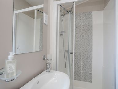 A bathroom with a sink mirror and shower enclosure with tiled wall at 97 Crugan in Llanbedrog