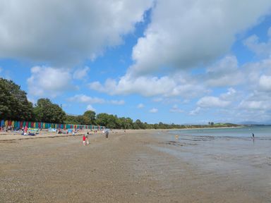 A sandy beach with people near colorful beach huts and trees at 97 Crugan in Llanbedrog