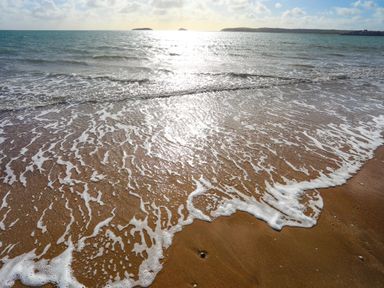 A sandy beach with waves washing ashore under a cloudy sky at 97 Crugan in Llanbedrog