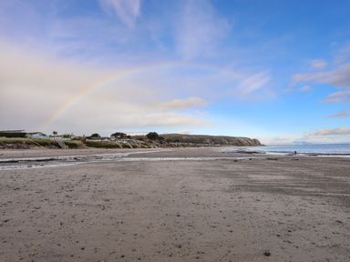 A sandy beach with houses along the shore and a rainbow in the sky at 97 Crugan in Llanbedrog
