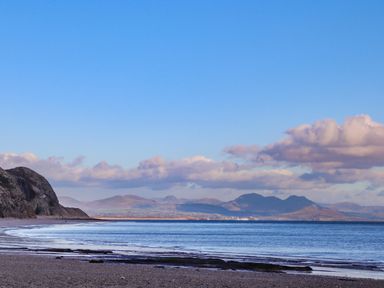 A beach with a rocky headland on the left and mountains in the distance at 97 Crugan in Llanbedrog