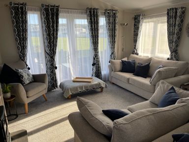 A living room with sofas and armchair by windows with patterned curtains at 97 Crugan Llanbedrog