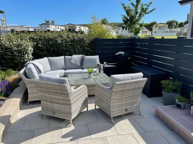 An outdoor seating area with wicker chairs and a sofa around a glass table on a tiled patio at 97 Crugan in Llanbedrog