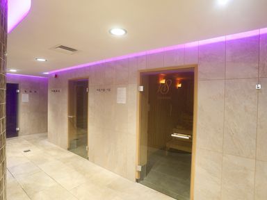 A hallway with beige tiled walls and floors purple LED lighting and glass doors leading to sauna rooms at 97 Crugan in Llanbedrog