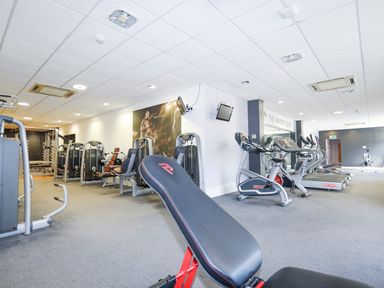 A gym with exercise bikes treadmills weight machines and benches at 97 Crugan in Llanbedrog