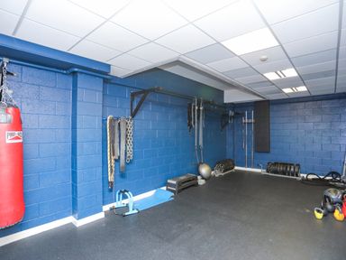 A gym room with blue walls containing a red punching bag, exercise mats, weights, kettlebells, and workout equipment at 97 Crugan in Llanbedrog