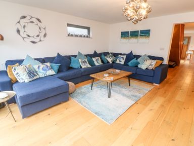 A living room with a large blue sectional sofa with multiple cushions a wooden coffee table and a wall decoration at Tregenna House in St Ives