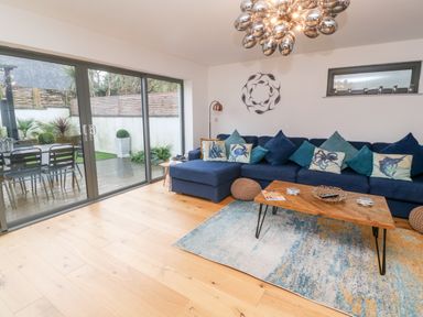 A living room with a blue sectional sofa and wooden coffee table next to glass sliding doors at Tregenna House in St Ives