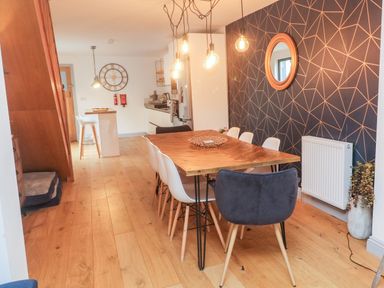 A dining area with a wooden table and chairs next to a kitchen with stools and a wall clock at Tregenna House in St Ives