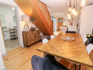 A dining room with a wooden table and white chairs near a staircase and a wooden cabinet at Tregenna House in St Ives