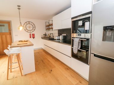 A kitchen with wooden floor white cabinets an island with stools a wall clock ovens and a refrigerator at Tregenna House in St Ives