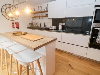 A kitchen with a wooden island and white bar stools a wall clock and shelves with cups at Tregenna House in St Ives