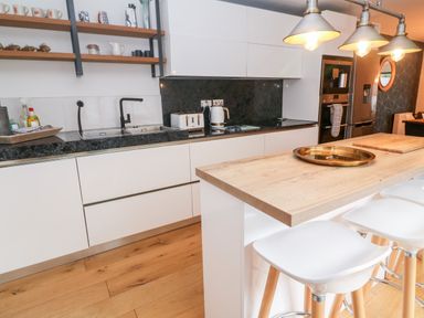 A modern kitchen with white cabinets a wooden countertop stools pendant lights and open shelves at Tregenna House in St Ives