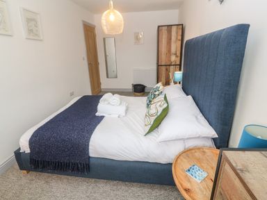 A bedroom with a blue upholstered bed a wooden side table with a lamp rolled towels and cushions at Tregenna House in St Ives